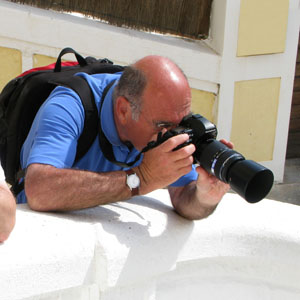 male photography leans on white wall to take a picture with a telephoto lens