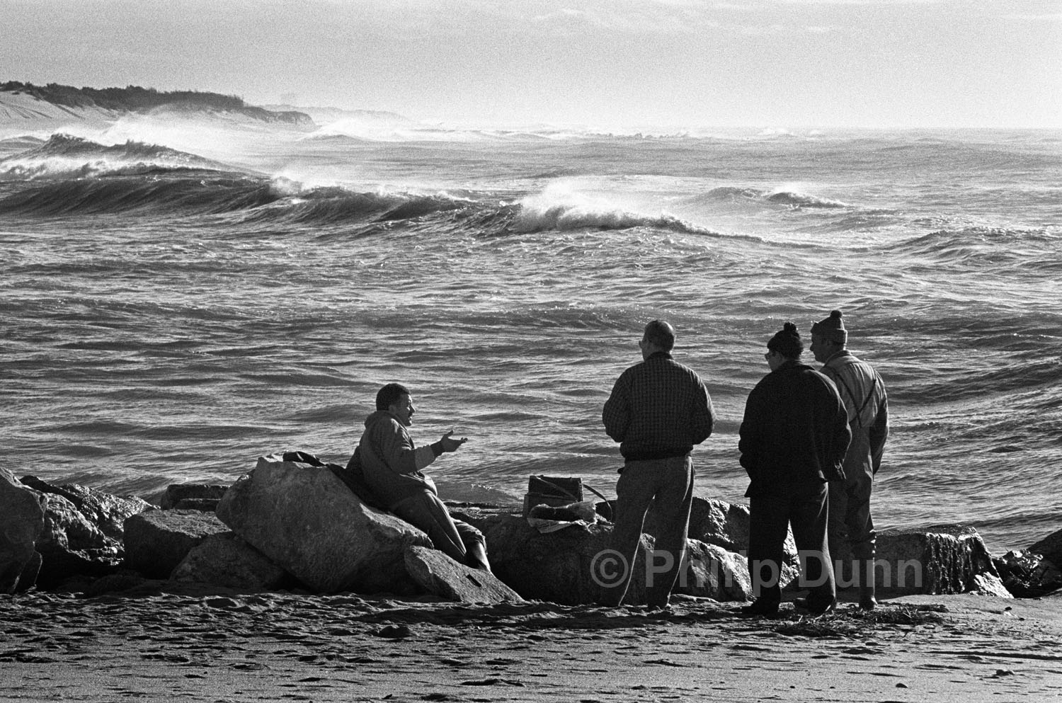 group of men talking beside huge waves off beach in Portugal