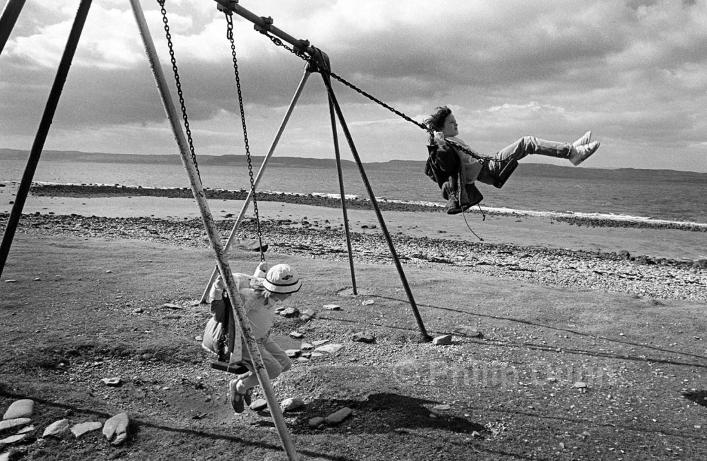 two girls on swing on Arran, Scotland. One girl swing high in the air
