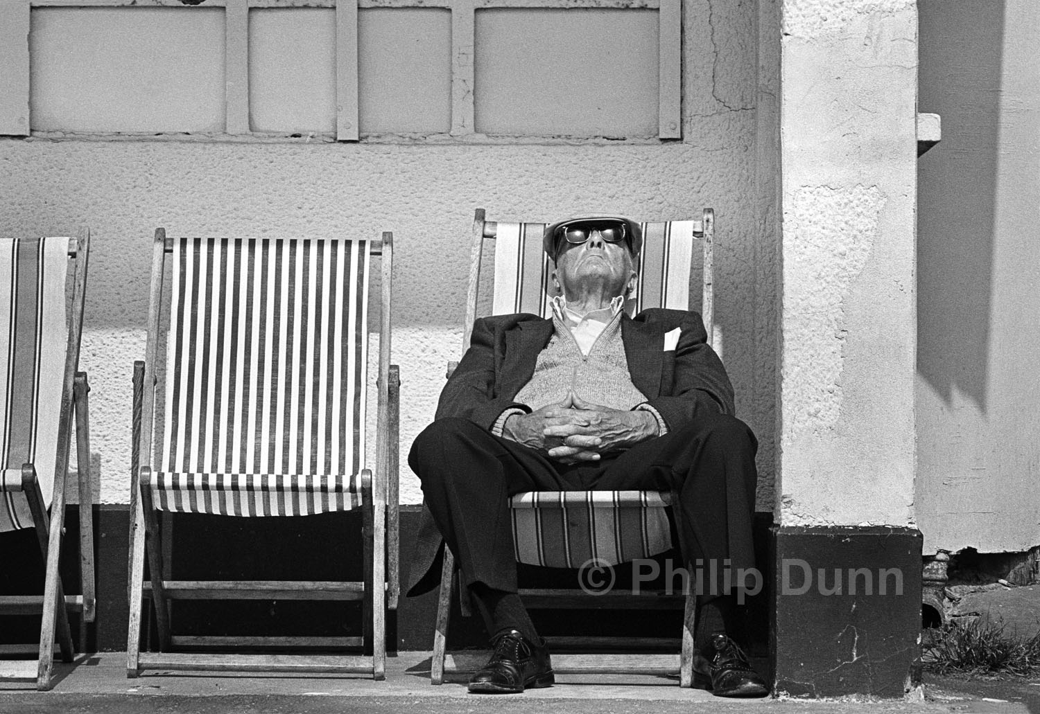 Old man wearing dark glasses and cloth cap, sleeps in deck chair