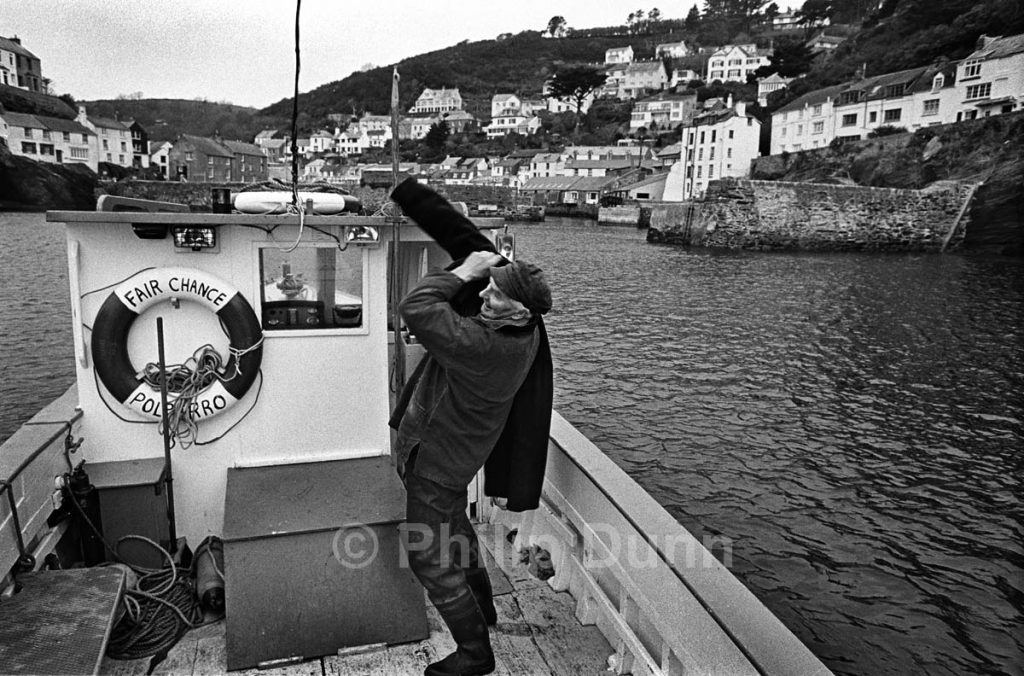 Fisherman prepares to go ashore after a day on his boat, Polperro harbour, Cornwall